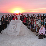 夕日をバックに砂で作ってくれた５０周年のモニュメントを囲んで記念撮影